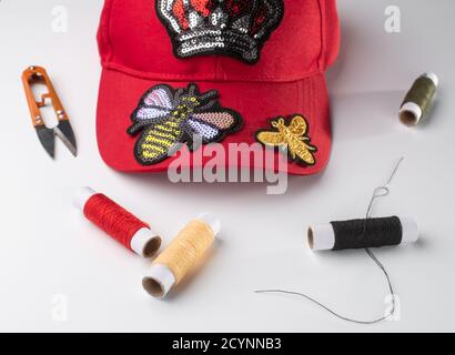 Rote Mütze mit verschiedenen Flecken, Fäden, Scheren und einer Neele auf weißem Hintergrund Stockfoto
