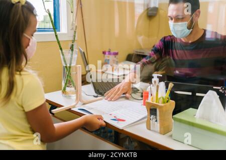 Schüler mit einer Maske, die Hausaufgaben an den Lehrer übergibt Durch einen Bildschirm Stockfoto