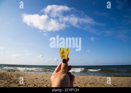 Bernstein im Sand vor dem Hintergrund der Meereswellen. Stockfoto