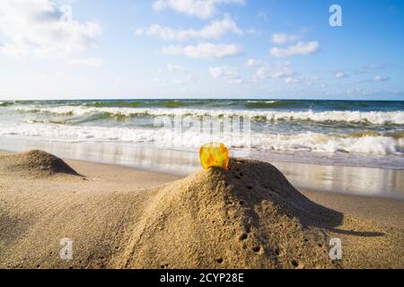 Bernstein im Sand vor dem Hintergrund der Meereswellen. Stockfoto