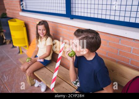 Kinder essen einen Apfel in der Aussparung sitzen auf einer Bank halten soziale Distanz. Stockfoto