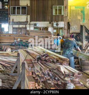 In einem Sägewerk im Industriegebiet Seguntor in Sandakan, Sabah, schneiden Arbeiter große Hölzer in Planken Stockfoto