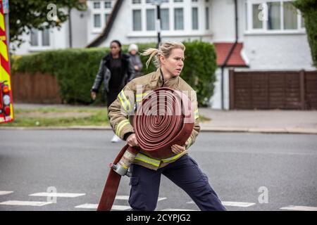 Die Feuerwehrfrau rollt den Schlauch mit der Londoner Feuerwehr aus, die an einem Hausbrand in einer Wohnstraße in South London, England, Großbritannien teilnimmt Stockfoto