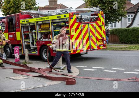 Die Feuerwehrfrau rollt den Schlauch mit der Londoner Feuerwehr aus, die an einem Hausbrand in einer Wohnstraße in South London, England, Großbritannien teilnimmt Stockfoto