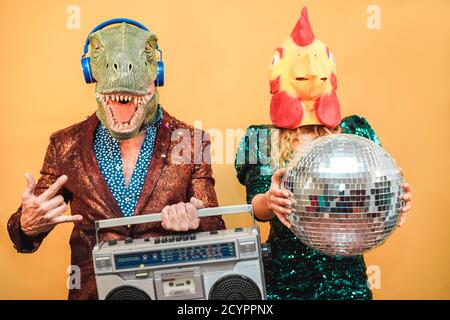 Verrückte stilvolle Menschen Musik hören mit vintage Boombox Stereo - Mode-Paar trägt T-rex und Hühnermaske auf Party-Fest Veranstaltung - absurd, holida Stockfoto