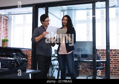 Gemischte Rasse Frau und kaukasischen Mann arbeiten in einem lässigen Büro, mit Tablet und diskutieren ihre Arbeit. Kreative Business-Profis arbeiten in einem BU Stockfoto