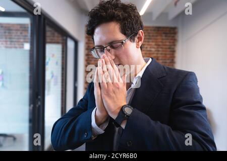 Kaukasischer Mann, der in einem legeren Büro arbeitet, niest und seine Nase bedeckt. Soziale Distanzierung am Arbeitsplatz während der Coronavirus Covid 19 Pandemie. Stockfoto