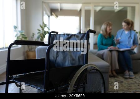 Ältere kaukasische Frau zu Hause von kaukasischen Krankenschwester besucht, sitzen auf der Couch, im Gespräch mit einem Rollstuhl im Vordergrund. Medizinische Versorgung zu Hause Dur Stockfoto