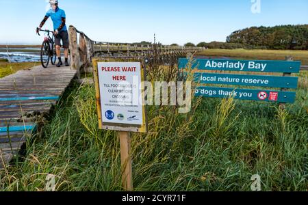 Aberlady Nature Reserve, East Lothian, Schottland, Großbritannien, 2. Oktober 2020. UK Wetter: Ein schöner sonniger Tag an der Küste. Besucher müssen sich an das einbahnige soziale Distanzierungssystem über die schmale hölzerne Fußgängerbrücke halten, während ein Radfahrer, der ein Fahrrad schiebt, die Brücke überquert Stockfoto