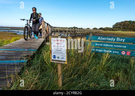 Aberlady Nature Reserve, East Lothian, Schottland, Großbritannien, 2. Oktober 2020. UK Wetter: Ein schöner sonniger Tag an der Küste. Besucher müssen sich an das einbahnige soziale Distanzierungssystem über die schmale hölzerne Fußgängerbrücke halten, während Radfahrer, die Fahrräder schieben, die Brücke überqueren Stockfoto