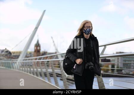 Eine Frau geht über die Friedensbrücke über den Fluss Foyle in Derry. Die Stormont-Exekutive kündigte am Donnerstag eine breite Reihe von Beschränkungen für die Derry City und Strabane Council Area in dem Bemühen, die Spirale Covid-19-Infektion Zahlen im Nordwesten von Nordirland einzudämmen. Stockfoto