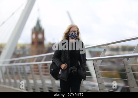 Eine Frau geht über die Friedensbrücke über den Fluss Foyle in Derry. Die Stormont-Exekutive kündigte am Donnerstag eine breite Reihe von Beschränkungen für die Derry City und Strabane Council Area in dem Bemühen, die Spirale Covid-19-Infektion Zahlen im Nordwesten von Nordirland einzudämmen. Stockfoto