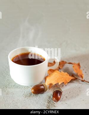 Tasse Eichel heißen Kaffee, Eicheln und gelbe Eichenblätter auf einem grauen Hintergrund. Ein gesundes hausgemachtes, umweltfreundliches Heißgetränk ohne Koffein Stockfoto