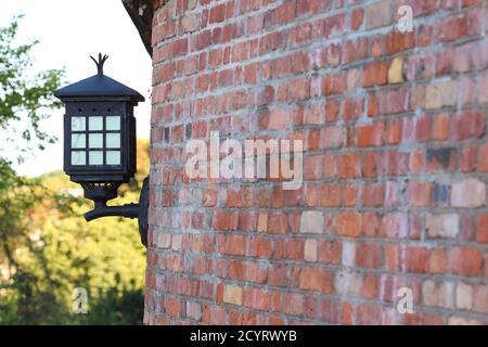 Alte elektrische Laterne aus Stahl, die an der roten Ziegelwand befestigt ist Stockfoto