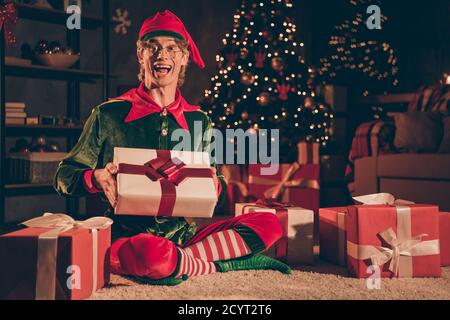 In voller Länge Foto von aufgeregt elf sitzen Boden mit Weihnachten weihnachts-Geschenkbox im Abendhaus im Innenbereich mit Wunderdekoration Leuchtet Stockfoto