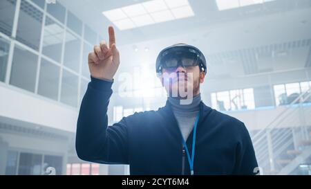 Automobilingenieur mit Augmented Reality Headset und Moving Virtual Pieces in the Air. In Innovation High Tech Laboratory Facility mit futuristischen Stockfoto