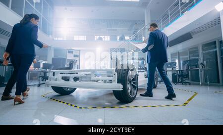 Automobil-Design-Ingenieure sprechen während der Arbeit an Elektro-Auto-Chassis-Prototyp. In Innovation Laboratory Facility Konzept Fahrzeug Rahmen Umfasst Stockfoto