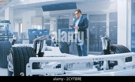 Automobilkonstrukteur mit Blick auf die technische Zeichnung eines Prototypen eines Elektroauto-Fahrgestells auf einem Tablet. In Innovation Laboratory Facility Konzept Stockfoto