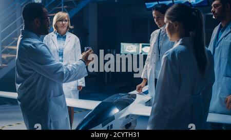 Treffen der Luft- und Raumfahrtingenieure, die am unbemannten Luftfahrzeug-Drohne-Prototyp arbeiten. Luftfahrtwissenschaftler in White Coats sprechen. Gewerbliches Luftbild Stockfoto