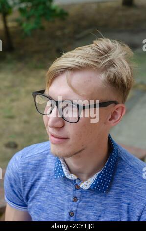 Porträt von stilvollen jungen Mann trägt eine Brille. Schöner junger Mann in stilvollen Gläsern mit modischer Frisur in modisch blauem Hemd posiert auf t Stockfoto
