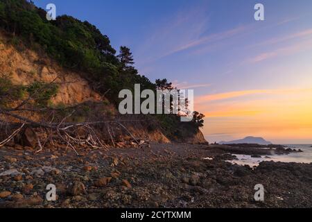 Ein wunderschöner Sonnenuntergang Himmel über einem steinigen Strand und Küstenklippen. Aufgenommen auf der Coromandel Peninsula, Neuseeland Stockfoto