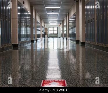 Ein leerer Schulflur mit einem Wegweiser auf dem Boden als Teil der neew normal für die Öffnung von Schulen in einer Pandemie geklebt. Stockfoto