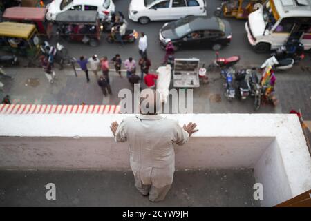 (Selektiver Fokus) EIN Mann indischer Ethnie beobachtet von einem Balkon aus den Verkehr auf den Straßen von Jaipu, Rajasthan, Indien Stockfoto