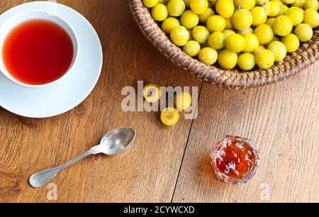 Eine Tasse schwarzen Tee, gelbe Mirabellepflaumen und Pflaumenkonfitüre auf einem Holztisch, Draufsicht Stockfoto