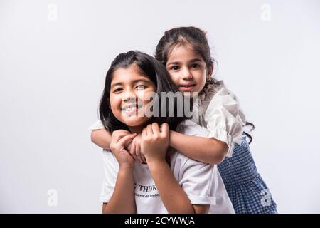 Nette kleine indische asiatische Geschwister stehen und umarmen einander in weißen Kleidern, während sie gegen weißen Hintergrund stehen. Stockfoto