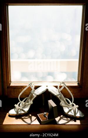 Brautsandalen auf einer hölzernen Fensterbank mit Eheringen in einer Schachtel. Stockfoto