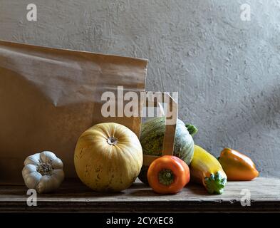 Bio frisches Gemüse - gelbe Zucchini, runde Zucchini, Paprika, Knoblauch und umweltfreundliche Papiertüte auf grauem Hintergrund. Kunststofffreies Einkaufen Stockfoto