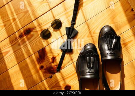 Herren schwarze Schuhe Tassel Slipper mit Fliege und Sonnenbrille auf Holzhintergrund. Stockfoto