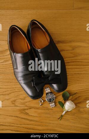 Schwarze Herrenschuhe und Fliege auf Holz Textur mit Manschettenknöpfen, Armbanduhr und weiß Rose Bräutigam boutonniere. Stockfoto