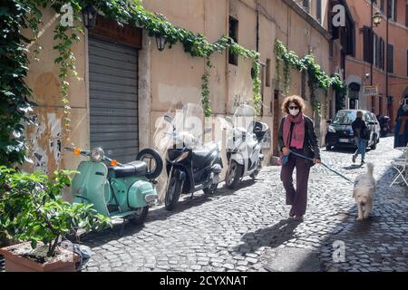 ROM, ITALIEN - OKTOBER 01 2020: Eine Frau schlendert ihren Hund entlang einer gepflasterten Straße in Rom, Italien. Stockfoto