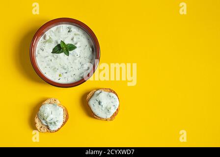 Eine Schüssel und Crostini oder Bruschetta mit traditionellen griechischen Tzatziki Sauce isoliert auf dem gelben Hintergrund Stockfoto