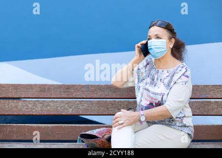 Reife Frau mit einer medizinischen Maske sprechen am Telefon. Sie ist draußen. Leerzeichen für Text. Stockfoto