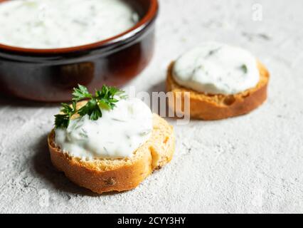 Crostini oder Bruschetta mit traditionellen griechischen Tzatziki-Sauce und ein Schüssel Nahaufnahme auf dem grauen Hintergrund Stockfoto