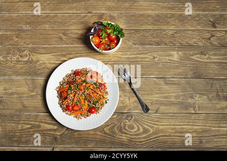 Gesunder vegetarischer Salat mit Buchweizen und Gemüse auf weißem Teller auf Holzhintergrund, Draufsicht mit Kopierraum Stockfoto