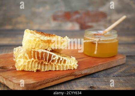 Honig in einem Glas und Wabe auf einem alten hölzernen Hintergrund. Stockfoto