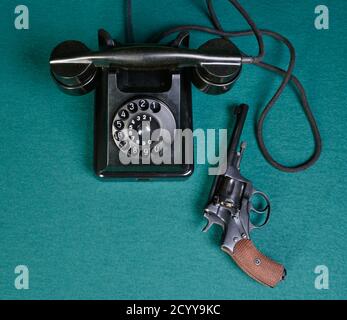 Auf einem grünen Tuch ein altes Telefon und ein altes Revolver Stockfoto