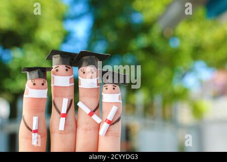 Finger Kunst von Studenten in medizinische Maske aus COVID-2019. Absolventen, die ihr Diplom nach dem Abschluss halten. Stockfoto