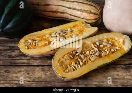 Drei Arten von Winter-Squash, Delicata Squash, Eichel-Squash und Butternut Squash, der Delicata Squash ist in zwei Hälften geschnitten, aus einem Winkel betrachtet, auf Holz Stockfoto