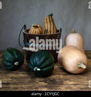 Drei Arten von Winter-Squash, Delicata Squash, Eichelkürbis und Butternut Squash und ein Eimer, von der Seite betrachtet, auf Holztisch, ganze Frucht, sti Stockfoto
