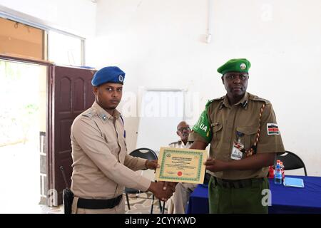 SSP. Francis Ndiema, Koordinator für Ausbildung und Planung der AMISOM-Polizei, überreicht einem Polizeibeamten während der Abschlussveranstaltung eines von den Polizeikomponenten der Mission der Afrikanischen Union in Somalia (AMISOM) organisierten Workshops zur gemeinschaftlichen Polizeiarbeit und Radikalisierung ein Zertifikat. Am 27. Juli 2019 in der General Kahiye Police Training Academy in Mogadischu, Somalia. Stockfoto