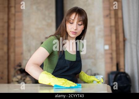 Schöne Frau in schwarzen Schürze Reinigungshaus, reibt Staub mit Mikrofaser Tuch Stockfoto