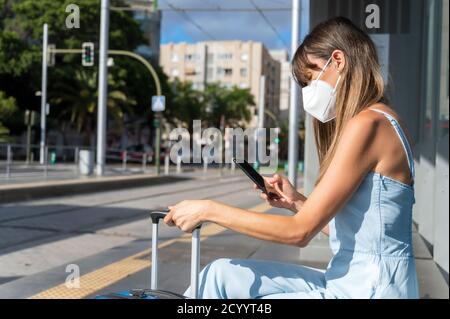 Pendeln in der Stadt während der neuen normalen. Frau mit Schutzmaske gegen Coronavirus Ausbruch wartet an der Straßenbahnhaltestelle. Hochwertige Fotos Stockfoto