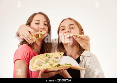 Zwei Mädchen essen Pizza auf weißem Hintergrund und lachen Stockfoto