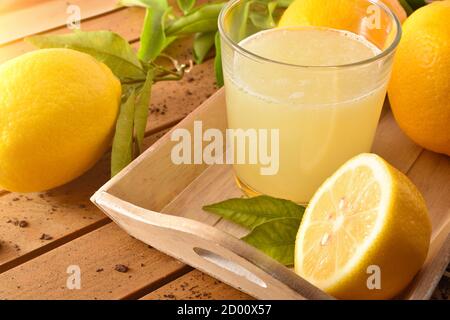 Frisch gepresster Saft auf einem Holztisch auf einem Tablett voller Zitronen. Erhöhte Ansicht. Horizontale Zusammensetzung. Stockfoto