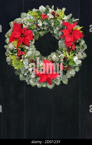 Weihnachtssterne Blume Thanksgiving & Weihnachtskranz mit schneebedeckter Tanne, Zeder, Stechpalme, Mistel & Tannenzapfen auf rustikalem dunklen Holz Hintergrund. Stockfoto