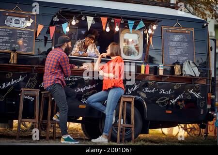 Hipster-Paar bei der Bestellung von Foodtruck auf der Straße; Urban Lifestyle-Konzept Stockfoto